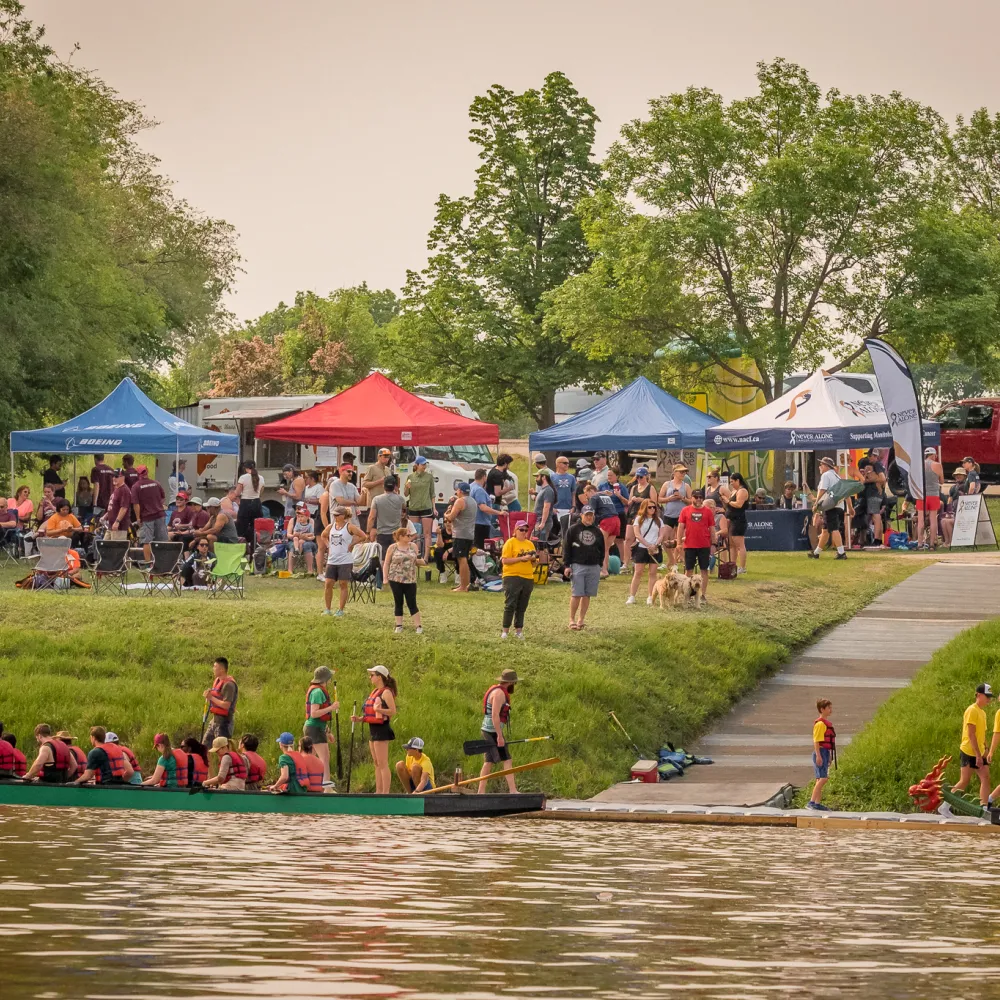 view from river towards the shore with dragon boats and tents
